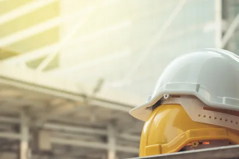 Zwei aufeinander gestapelte Schutzhelme vor einer Baustelle, symbolisch für Betriebsprüfung. © Shutterstock, FLUKY FLUKY