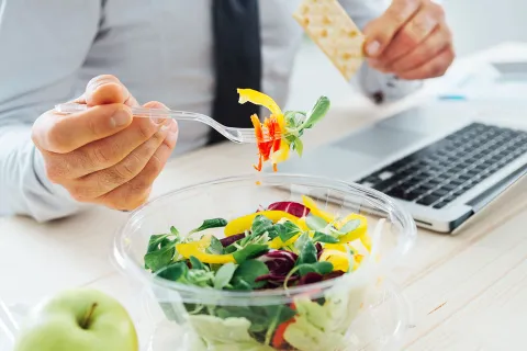 Mitarbeiter achtet auf gesunde Ernährung und isst einen Salat und einen Apfel am Arbeitsplatz. © Shutterstock, Stock-Asso