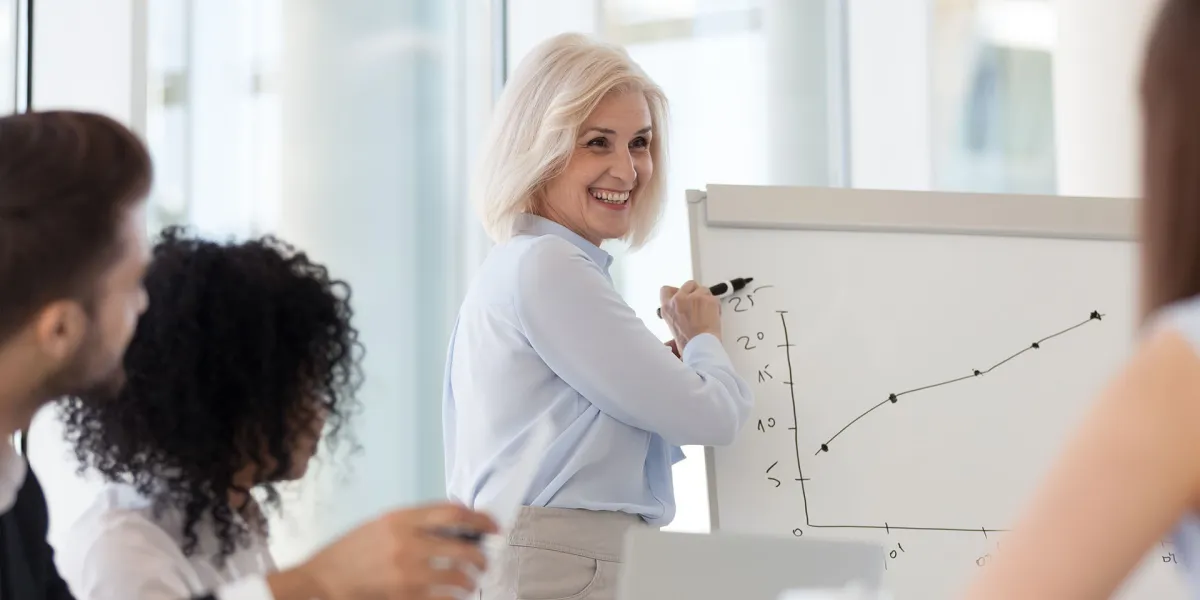 Unternehmerin erklärt an Whiteboard, wie das Team die Unternehmensvorsätze erfolgreich umsetzen kann. © Shutterstock, fizkes