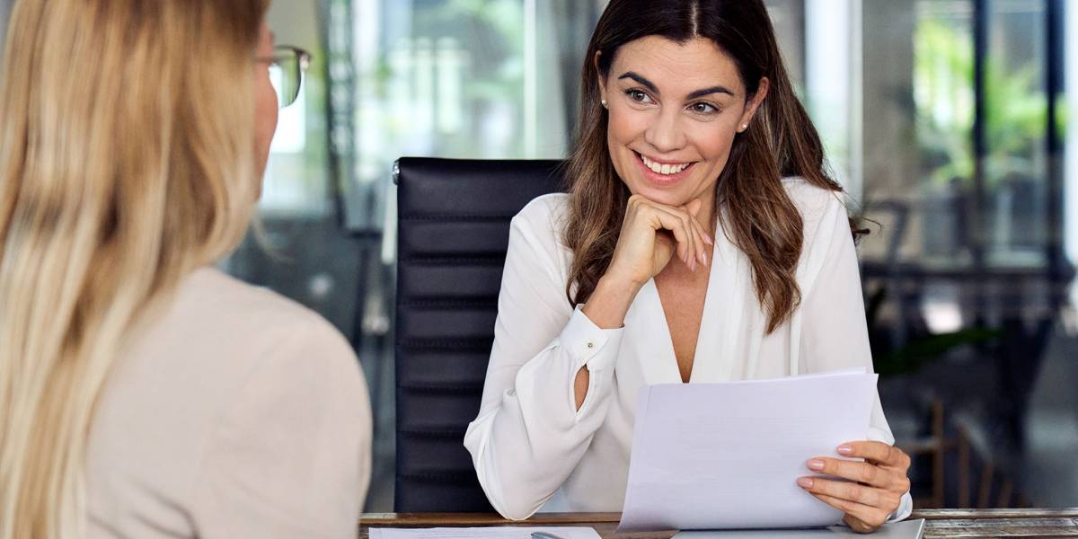 Lächelnde Frau mit weißen Bluse führt ein BEM-Gespräch in modernem Büro und hält dabei Unterlagen in der Hand.