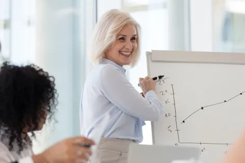 Unternehmerin erklärt an Whiteboard, wie das Team die Unternehmensvorsätze erfolgreich umsetzen kann. © Shutterstock, fizkes