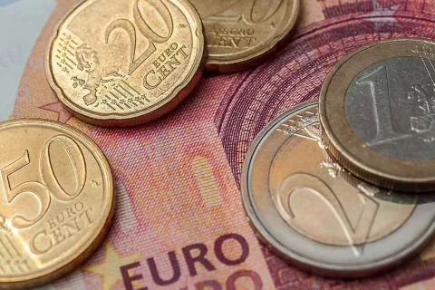 Mehrere Euro Münzen liegen auf einem Zehn Euro Geldschein als Symbol für den Anstieg des Mindestlohns.