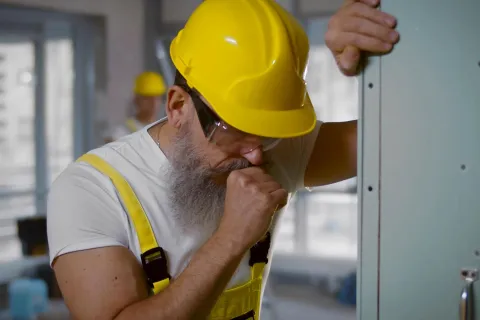 Ein Bauarbeiter hustet, da er die Berufskrankheit Asbestose hat. © Adobe Stock, nimito