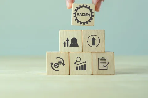 Finger heben einen Würfel mit der Aufschrift "Kaizen" von einer Würfelpyramide. © Adobe Stock, Parradee