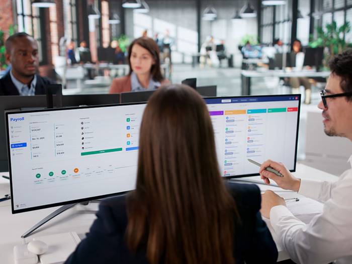 Team im Büro bespricht digitale Zeiterfassung auf Computerbildschirm zur Dokumentation von Arbeitsstunden und Mindestlohnregelungen.