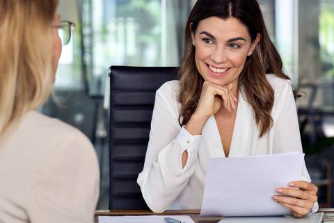 Lächelnde Frau mit weißen Bluse führt ein BEM-Gespräch in modernem Büro und hält dabei Unterlagen in der Hand.