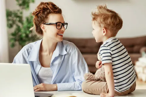 Eine Mutter vereinbart Beruf und Familie und lächelt beim Arbeiten ihr Kind an. © Adobe Stock, JenkoAtaman