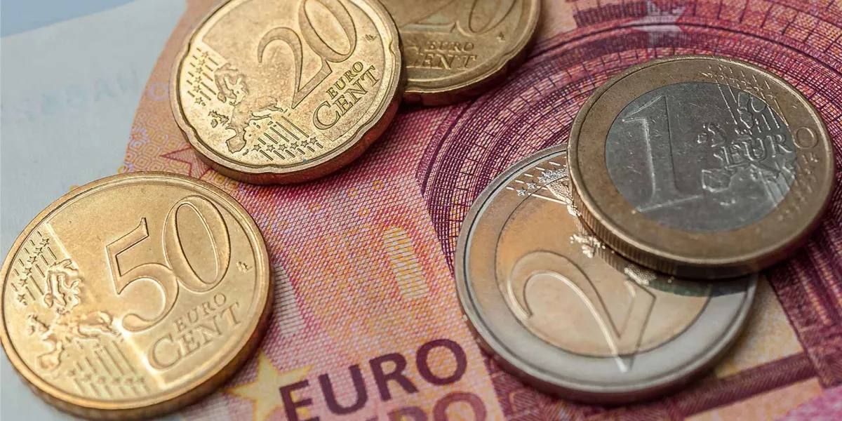 Mehrere Euro Münzen liegen auf einem Zehn Euro Geldschein als Symbol für den Anstieg des Mindestlohns.