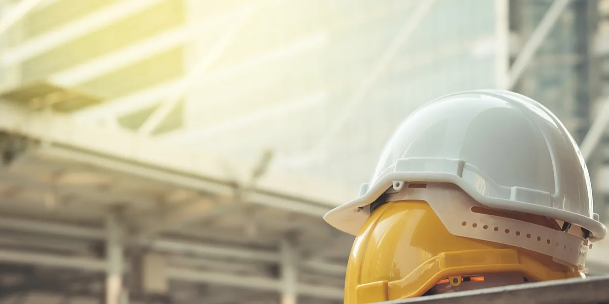 Zwei aufeinander gestapelte Schutzhelme vor einer Baustelle, symbolisch für Betriebsprüfung. © Shutterstock, FLUKY FLUKY