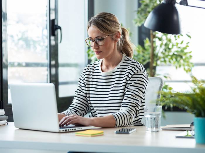 Person arbeitet konzentriert im Homeoffice an einem Laptop, umgeben von Pflanzen und Arbeitsmaterialien.
